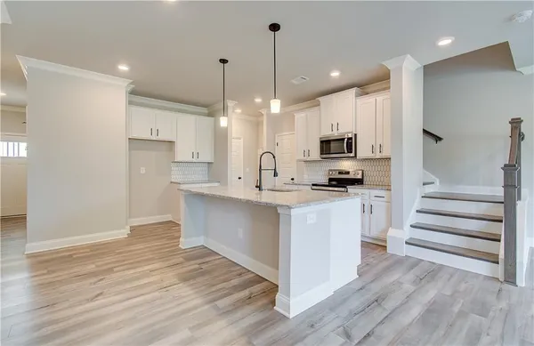a kitchen with kitchen island microwave stove refrigerator and white cabinets with wooden floor