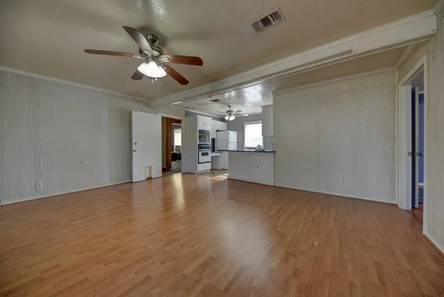 a view of an empty room with wooden floor and a ceiling fan