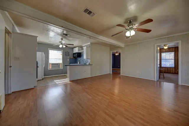 a view of an empty room with wooden floor and a kitchen