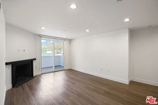 a view of an empty room with wooden floor fireplace and a window