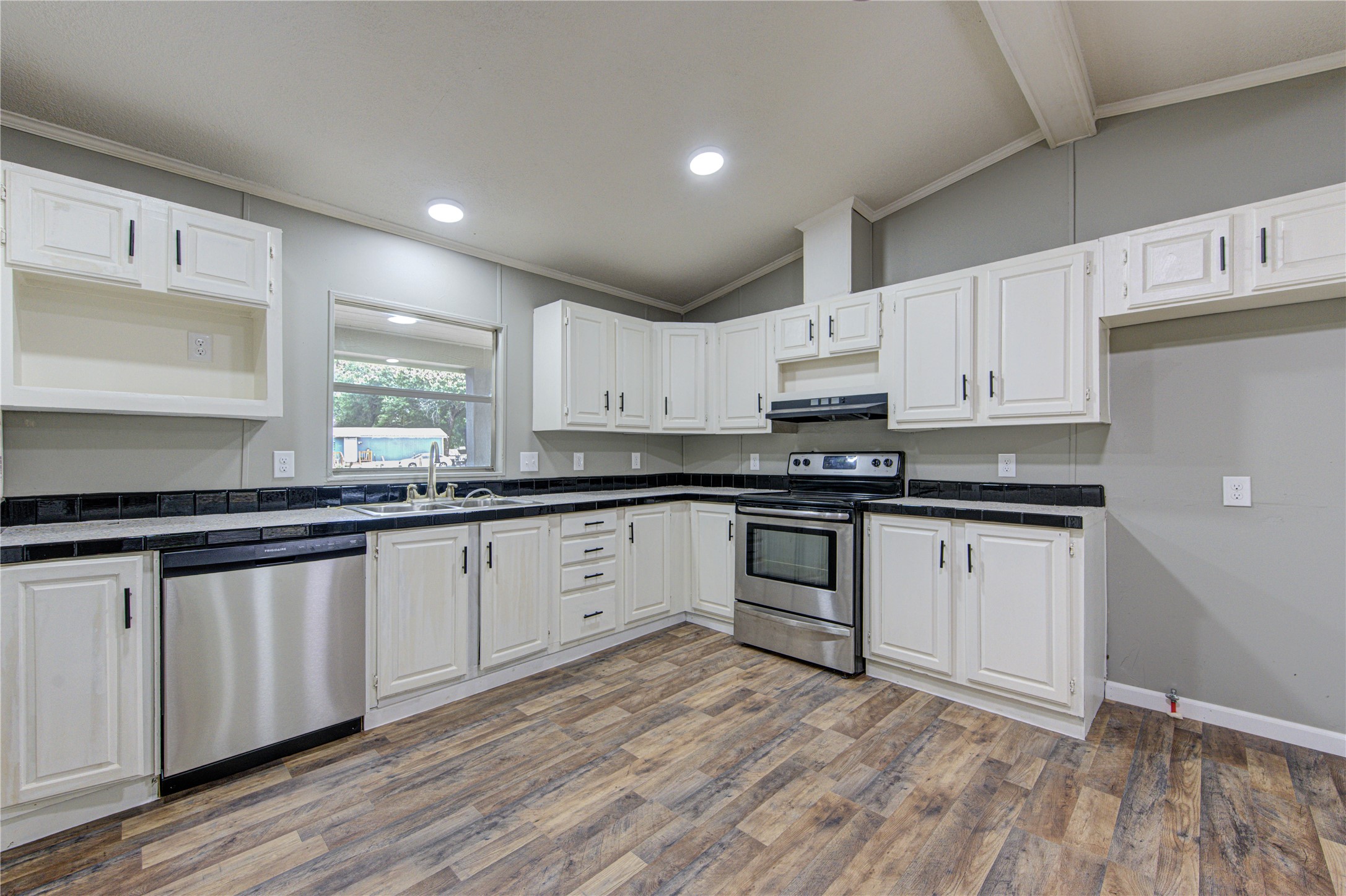 30226 Davis Street Magnolia, TX 77355 - Photo 19 of 50 This kitchen features a modern design with stainless steel appliances, white cabinetry, and a wood-look floor. The space is well-lit with recessed lighting and has ample counter space, including a window above the sink offering natural light.