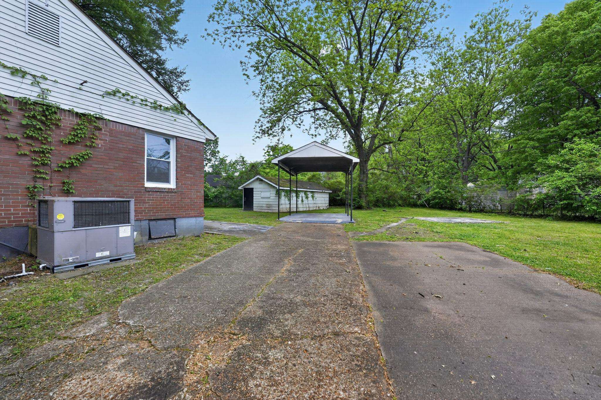 4067 Grantham Road Memphis, TN 38109 - Photo 4 of 34 View of green lawn with a carport, an outdoor structure, and asphalt driveway