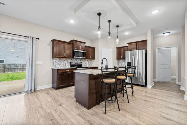 a kitchen with stainless steel appliances kitchen island granite countertop a refrigerator a stove a microwave oven a sink with island and chairs with wooden floor