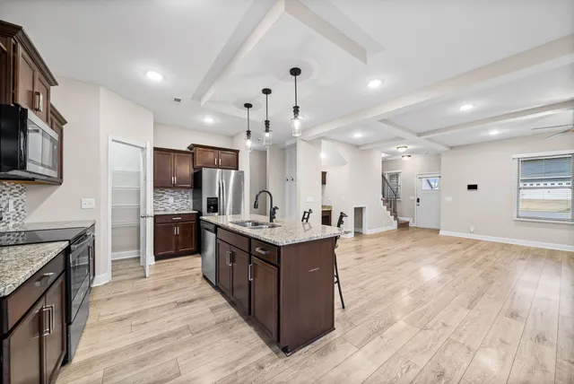 a kitchen with stainless steel appliances kitchen island granite countertop a stove top oven a sink dishwasher and a refrigerator with wooden floor