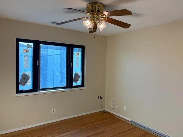 an empty room with wooden floor fan and windows