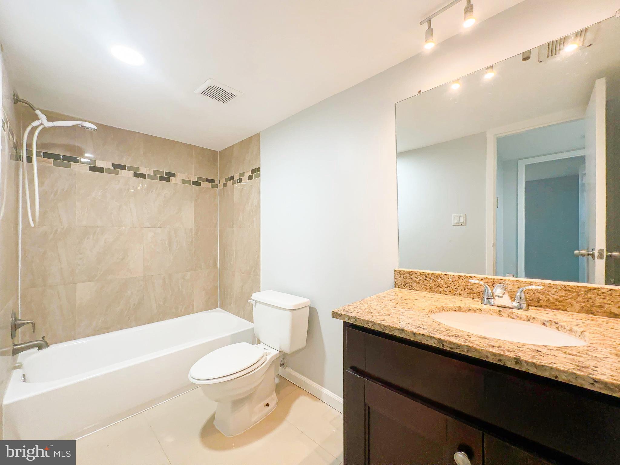 8671 Greenbelt Road, Unit 101 Greenbelt, MD 20770 - Photo 14 of 14 a bathroom with a granite countertop sink toilet a large mirror a bathtub and shower