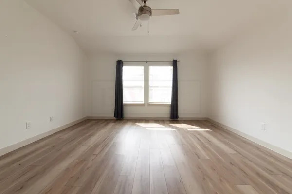 an empty room with wooden floor chandelier fan and windows