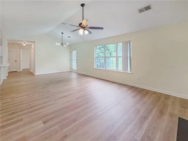 an empty room with wooden floor chandelier and windows