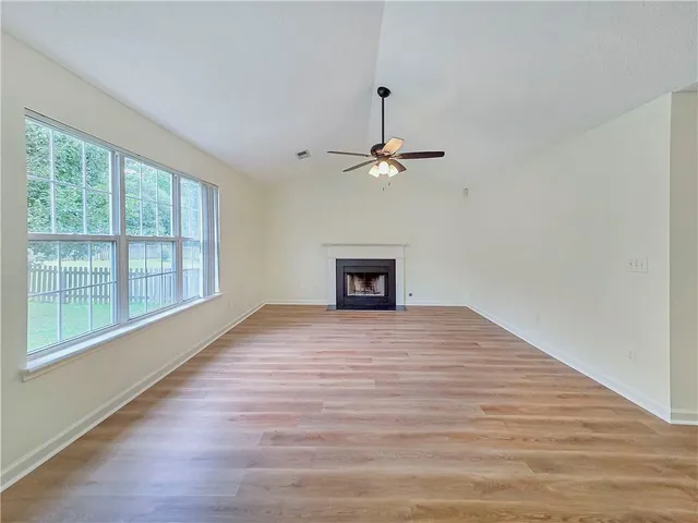 a big room with wooden floor a ceiling fan and windows