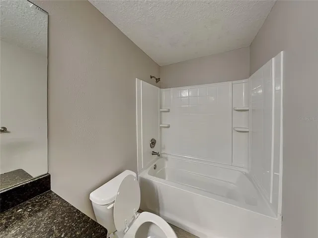 a bathroom with a granite countertop bathtub shower sink vanity and toilet
