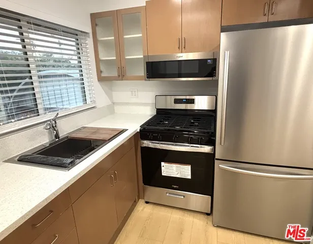 a kitchen with stainless steel appliances granite countertop a stove a refrigerator and a sink with wooden cabinets