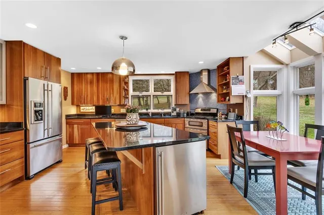 a kitchen with stainless steel appliances granite countertop a stove a refrigerator a kitchen island a stove a dining table and chairs with wooden floor