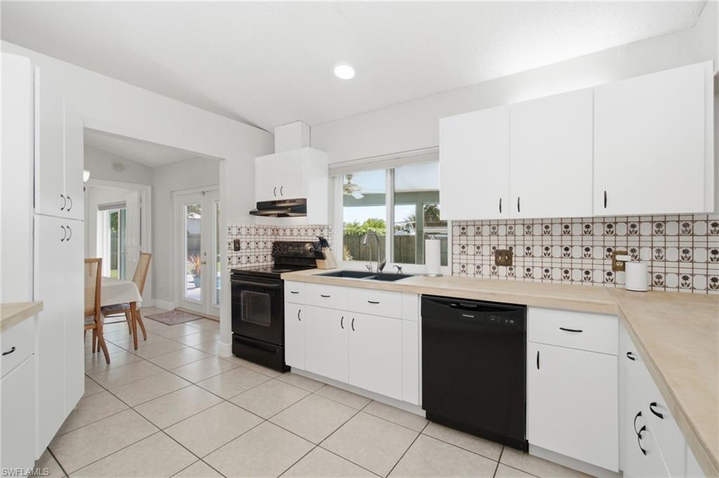 3022 47th Street Southwest Naples, FL 34116 - Photo 16 of 46 Kitchen featuring white cabinetry with dark hardware, black appliances, light-toned countertops, and a patterned tile backsplash