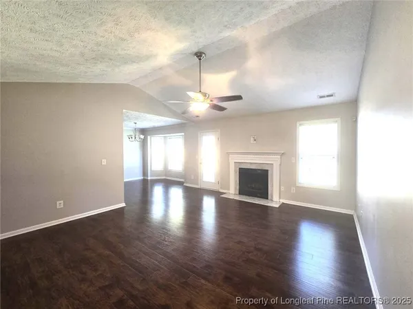 an empty room with wooden floor chandelier fan and windows