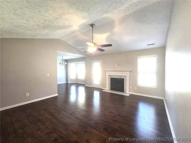 an empty room with wooden floor chandelier fan and windows