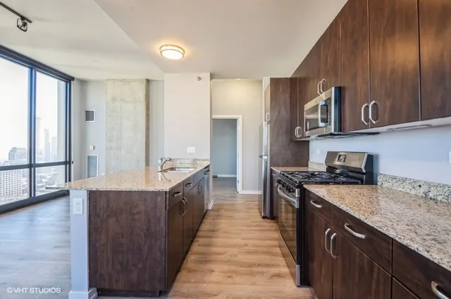 a large kitchen with stainless steel appliances granite countertop a large counter top a wooden floors and a large window