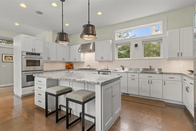 a kitchen with stainless steel appliances granite countertop a stove a sink dishwasher a refrigerator white cabinets and a wooden floor