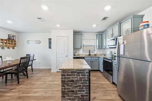 a kitchen with stainless steel appliances granite countertop a refrigerator a stove a sink a dining table and chairs