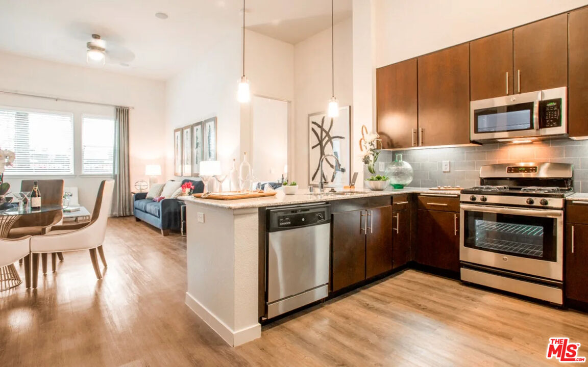 a kitchen with stainless steel appliances kitchen island granite countertop a stove top oven a sink dishwasher a dining table and chairs with wooden floor