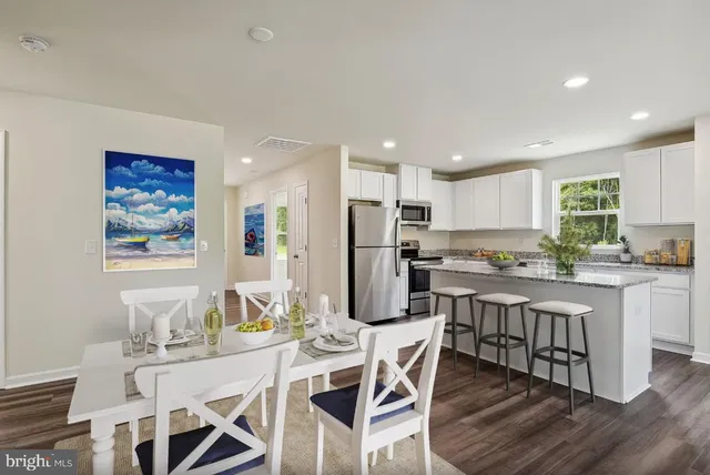 a kitchen with stainless steel appliances kitchen island granite countertop a dining table chairs and a refrigerator