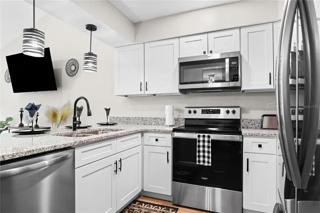 a kitchen with stainless steel appliances granite countertop a refrigerator a stove a sink and white cabinets