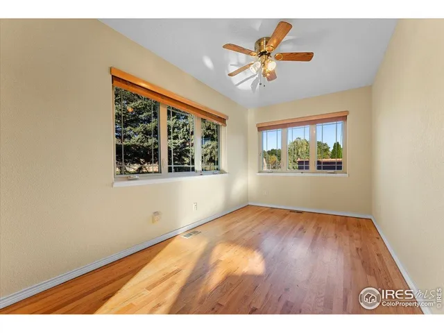 an empty room with wooden floor chandelier fan and windows
