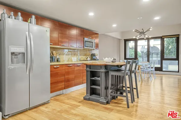 a kitchen with stainless steel appliances granite countertop a refrigerator a sink a stove and white cabinets with wooden floor