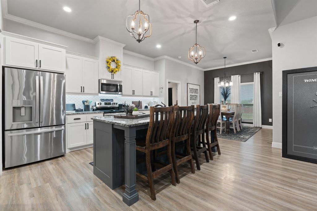 121 Treys Way Godley, TX 76044 - Photo 11 of 32 a kitchen with stainless steel appliances kitchen island granite countertop a refrigerator a stove a microwave oven a dining table and chairs with wooden floor