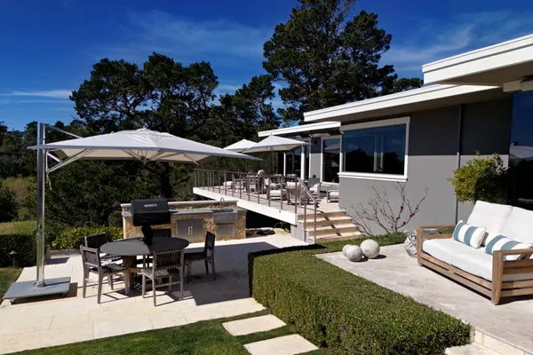 a view of a patio with couches table and chairs under an umbrella with a barbeque grill and plants