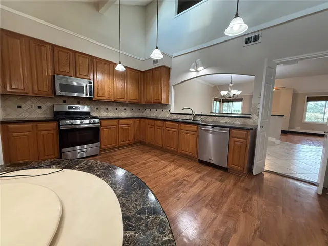a kitchen with stainless steel appliances granite countertop wooden cabinets a sink a stove a refrigerator and island