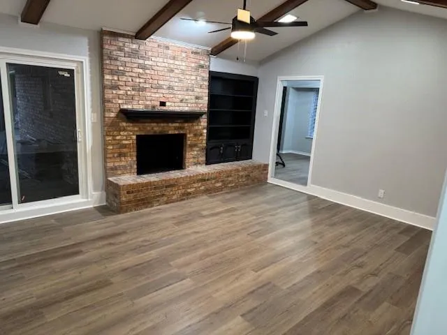 a view of an empty room with wooden floor fireplace and a window
