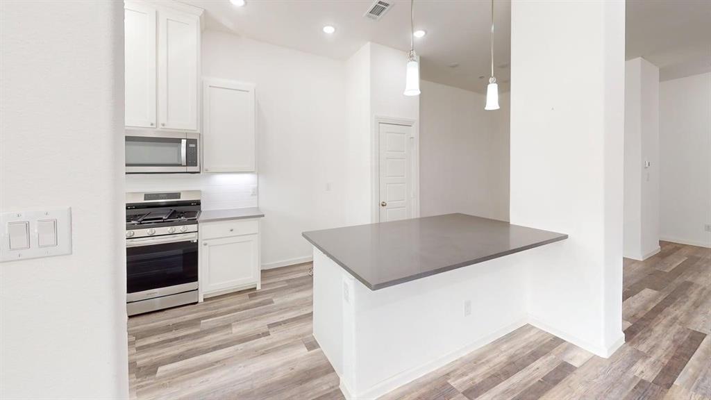 346 Buck Ridge Drive Frisco, TX 75068 - Photo 5 of 19 Kitchen featuring stainless steel appliances, white cabinets, light wood finished floors, and hanging light fixtures