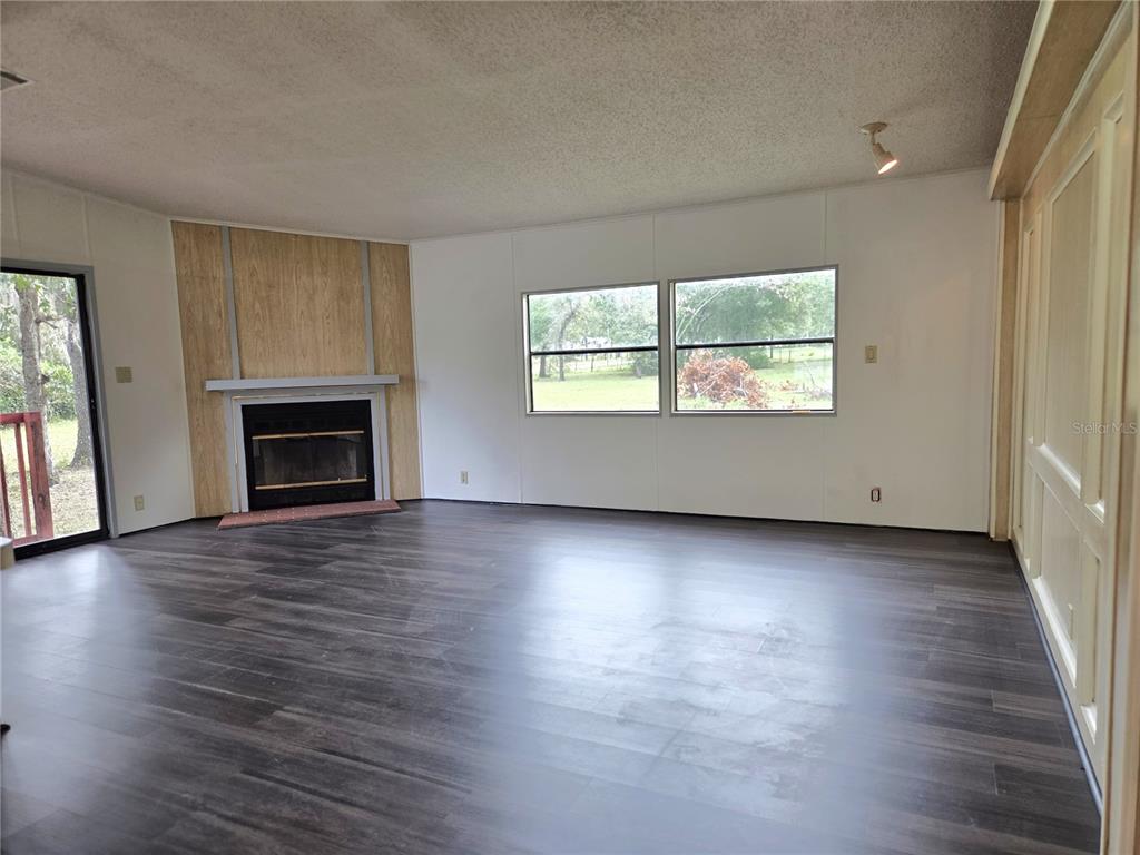 14822 Dilbeck Drive Spring Hill, FL 34610 - Photo 6 of 40 an empty room with wooden floor fireplace and windows