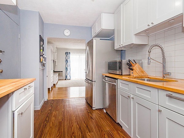 a kitchen with granite countertop a refrigerator a sink dishwasher and white cabinets with wooden floor