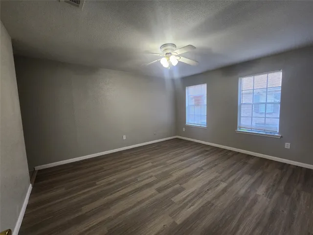 an empty room with wooden floor chandelier fan and windows