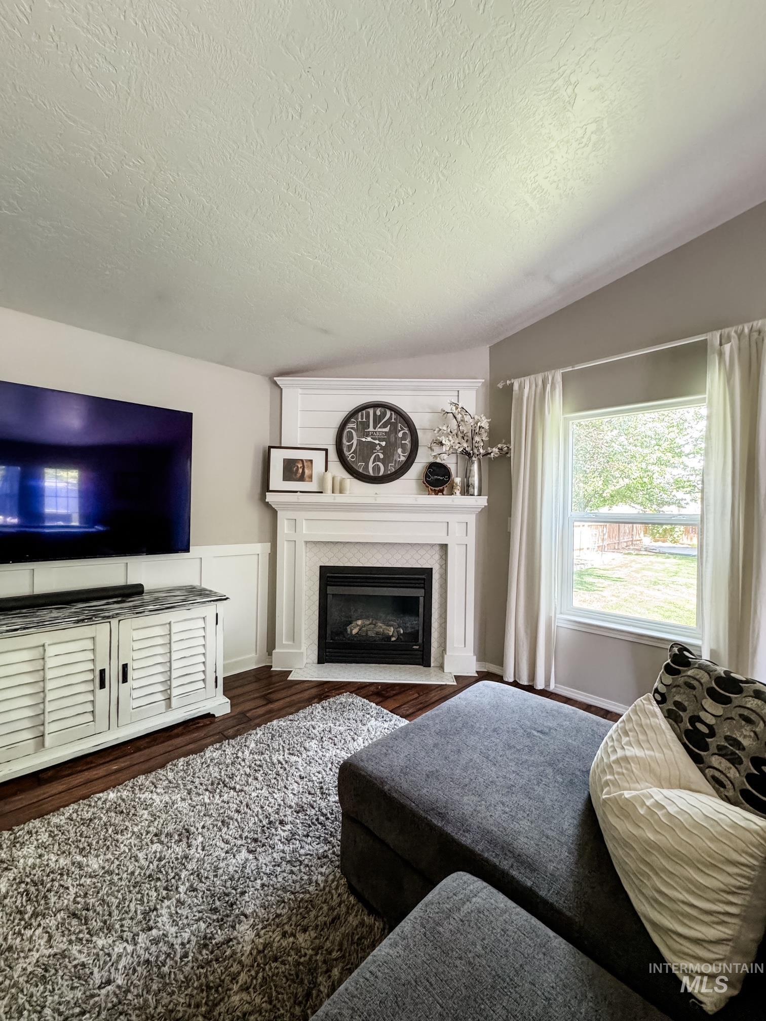 808 O'Leary Way Twin Falls, ID 83301 - Photo 7 of 37 Corner fireplace with a white mantel and tiled surround, hardwood flooring, and a large window providing natural light