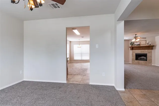 an empty room with chandelier fan and kitchen view