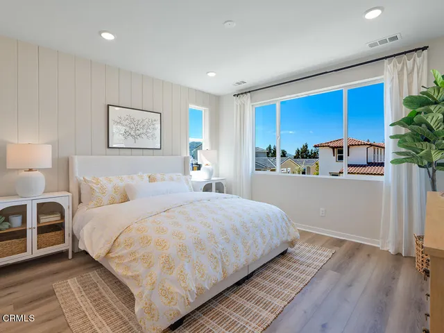 a bedroom with a large bed and potted plant with wooden floor
