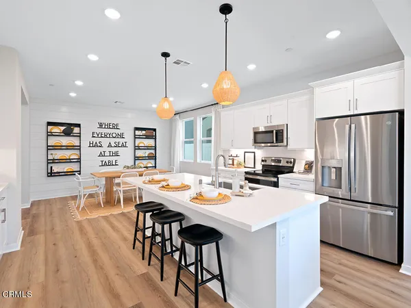 a kitchen with stainless steel appliances kitchen island granite countertop a dining table chairs stove refrigerator and cabinets