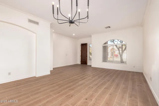 an empty room with wooden floor chandelier fan and windows