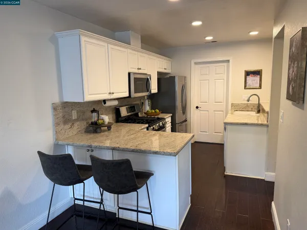 a kitchen with stainless steel appliances granite countertop a stove a refrigerator a sink a dining table and chairs with wooden floor