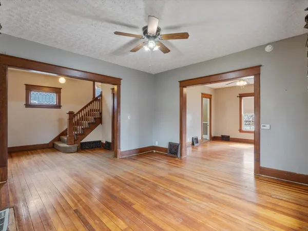a view of an empty room with wooden floor and a ceiling fan