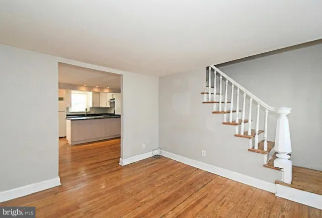 a view of empty room with wooden floor and kitchen