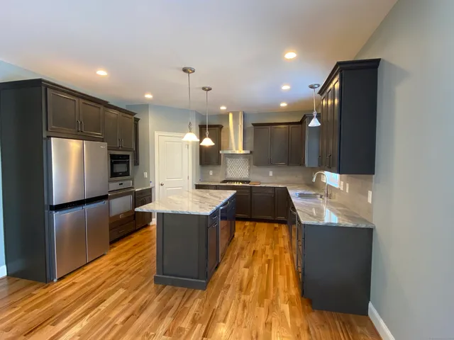 a kitchen with kitchen island granite countertop a refrigerator a sink a stove and wooden floor