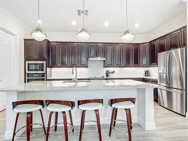 a kitchen with stainless steel appliances granite countertop a stove top oven a refrigerator a sink and chairs