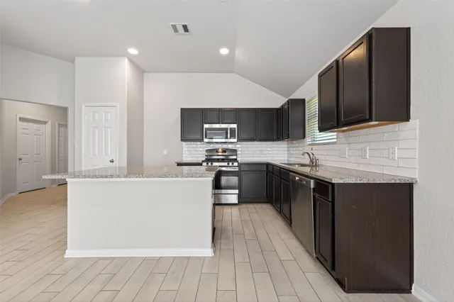 a large kitchen with stainless steel appliances kitchen island granite countertop a stove a sink dishwasher and a microwave oven on the wooden floor