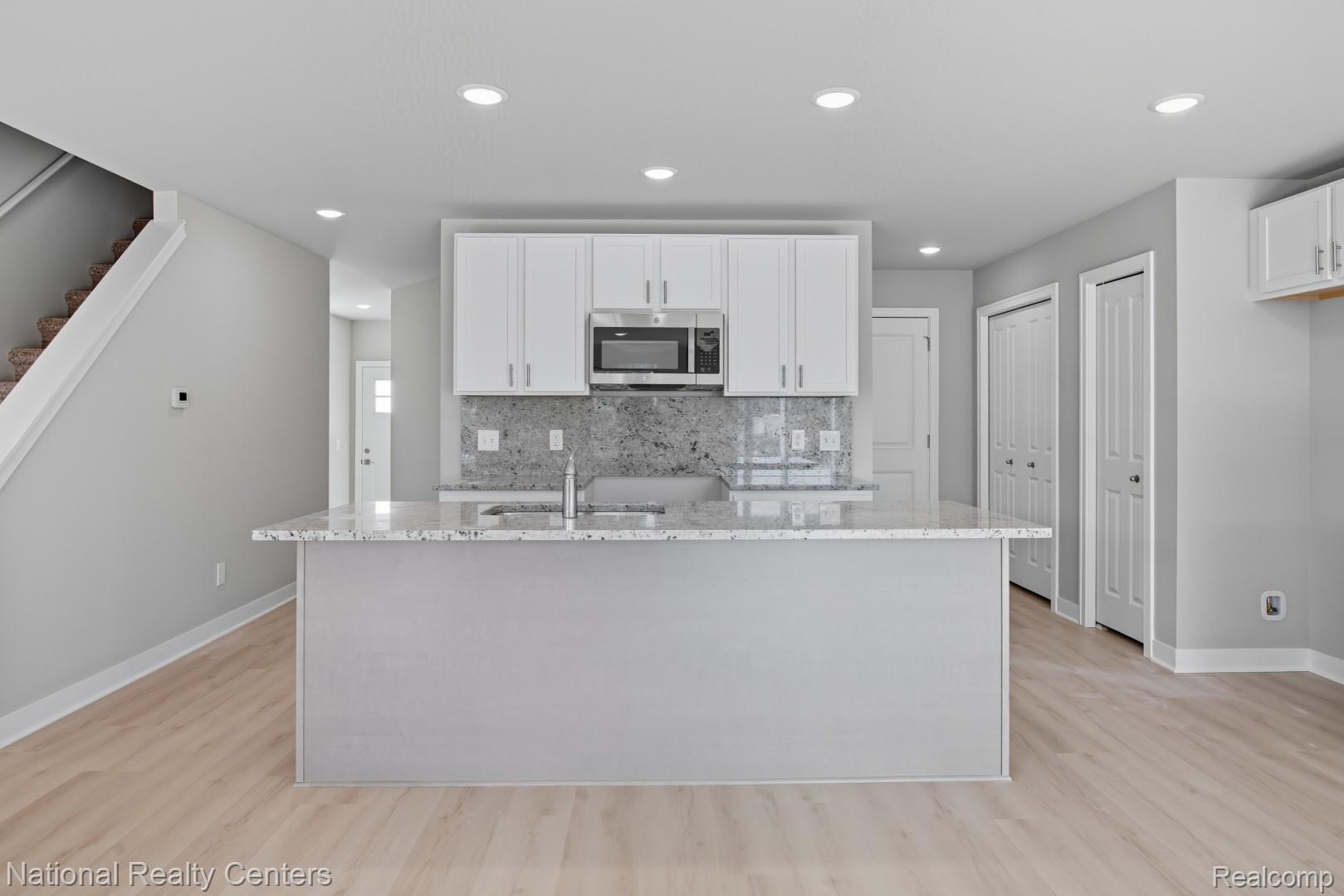 Kitchen island with a light-toned countertop, white cabinetry, integrated microwave, and a gray-toned backsplash