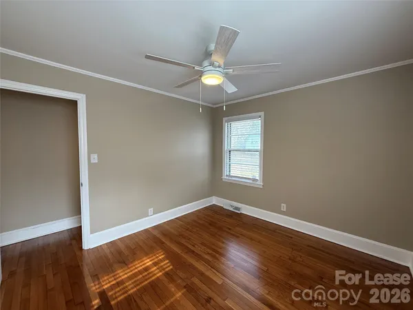 an empty room with wooden floor fan and windows