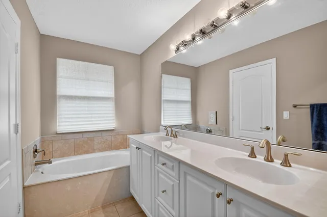 a bathroom with a double vanity sink large mirror and a bathtub
