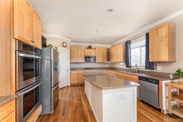 a kitchen with stainless steel appliances granite countertop a refrigerator a sink dishwasher a stove and white countertops with wooden floor